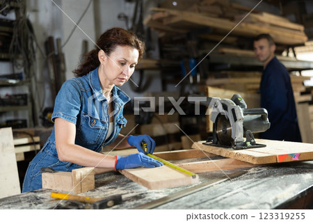 Work in woodworking enterprise - woman measures length of wooden board with tape measure Work in woodworking enterprise - woman measures length of wooden board with tape measure 123319255