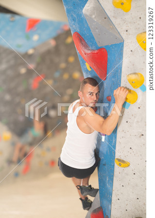 Atlete man grabbing ledges of artificial climbing wall in bouldering centre Atlete man grabbing ledges of artificial climbing wall in bouldering centre 123319267