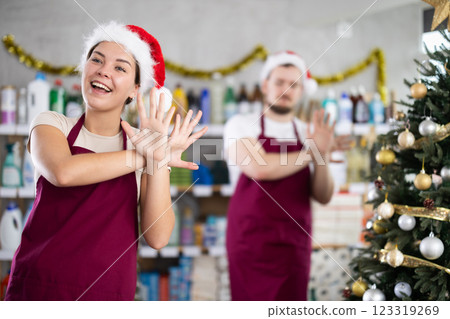 Cheerful sellers in Christmas clothes and a Santa hat dancing and fooling around behind the food counter. Supermarket workers wish Happy New Year Cheerful sellers in Christmas clothes and a Santa hat dancing and fooling around behind the food counter. Supermarket workers wish Happy New Year 123319269