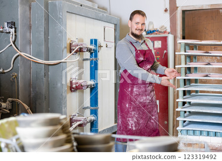 Young man posing at rack with ceramic dishes Young man posing at rack with ceramic dishes 123319492