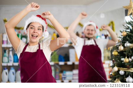 Cheerful happy two sellers in festive hats playfully dancing in hardware store decorated for New Year celebration Cheerful happy two sellers in festive hats playfully dancing in hardware store decorated for New Year celebration 123319518