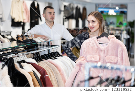 Girl stopped near showcase with outerwear, holds fur coat hanger in hands and examines product 123319522