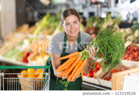 Girl supermarket worker with bunches of carrots in hands examines product Girl supermarket worker with bunches of carrots in hands examines product 123319526
