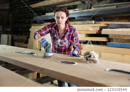 During manufacturing, woman employee grinds surface of wooden board, gives smoothness to surface 123319544