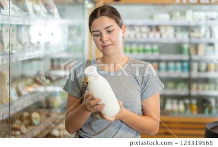 Positive young girl purchaser choosing milk in large supermarket 123319568