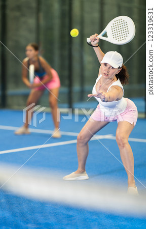 Woman with racket training on outdoor court playing padel game and hitting ball 123319631