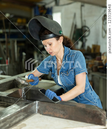 Portrait of a female welder standing with a welding semi-automatic machine and a safety helmet in metal machining workshop 123319648