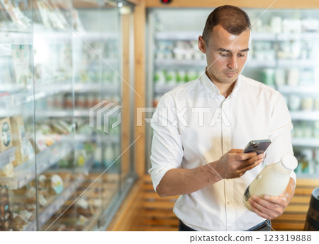 Attentive young man scanning QR code on milk bottle in large supermarket 123319888