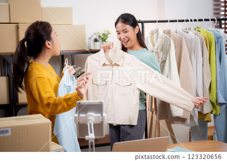 Two young asian woman live online clothing store while showing clothing with tablet on social. Two young asian woman live online clothing store while showing clothing with tablet on social. 123320656