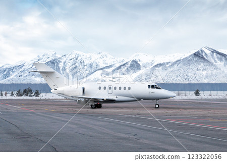 Taxiing of white luxury business jet on airport in winter on the background of high scenic snow capped mountains 123322056