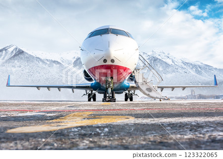 Front view of the modern luxury corporate business jet with open gangway door on the winter airport apron on the background of high scenic mountains 123322065