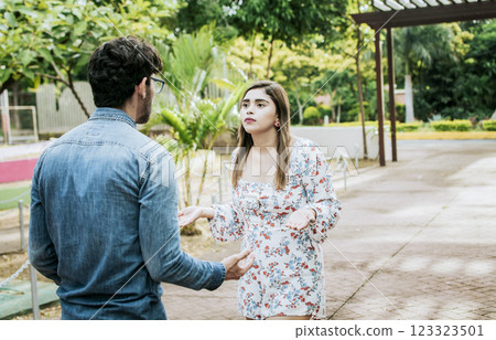 Unhappy couple standing arguing in a park. Disgusted teenage couple arguing in a park, Man and woman arguing in a park. Young couple arguing misunderstanding in a park Unhappy couple standing arguing in a park. Disgusted teenage couple arguing in a park, Man and woman arguing in a park. Young couple arguing misunderstanding in a park 123323501