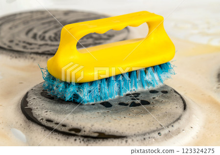 Close-up of a yellow and blue brush scrubbing a dirty stovetop with soapy water. Cleaning, chores, and home hygiene concept Close-up of a yellow and blue brush scrubbing a dirty stovetop with soapy water. Cleaning, chores, and home hygiene concept 123324275