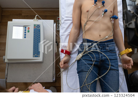 A female doctor performs an ECG on a young man in a hospital room, carefully monitoring his heart health during a routine checkup. 123324504