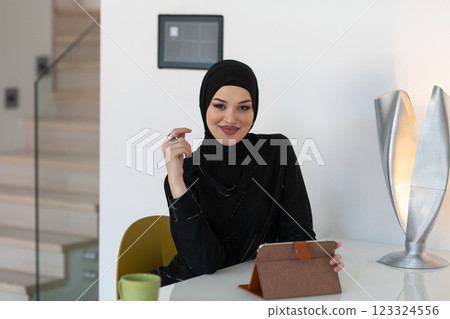Modern Muslim woman in a hijab working on a tablet at home. Modern Muslim woman in a hijab working on a tablet at home. 123324556