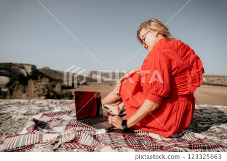 Young Woman in Red Dress Using Laptop on a Mountaintop Young Woman in Red Dress Using Laptop on a Mountaintop 123325663