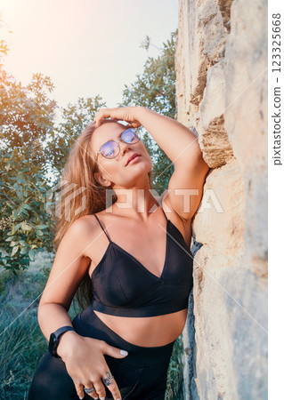 Woman Sunglasses Outdoors Posing - A woman wearing sunglasses poses outdoors against a stone wall. 123325668