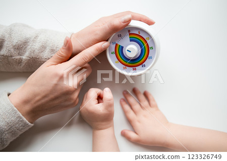 Adult and child hands adjusting colorful kitchen timer on white surface Adult and child hands adjusting colorful kitchen timer on white surface 123326749