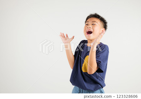 A jubilant kid boy raises her fists in celebration of her success, saying yes with excitement. Asian portrait of a happy young primary child in a studio shot on a white background, winning 123328606