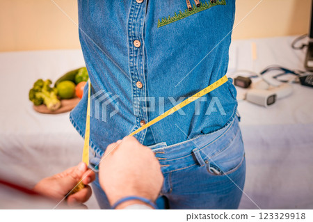 View of a male nutritionist measuring female patient waist. Concept of weight loss and professional nutritionist. Close-up of nutritionist measuring waist to patient View of a male nutritionist measuring female patient waist. Concept of weight loss and professional nutritionist. Close-up of nutritionist measuring waist to patient 123329918