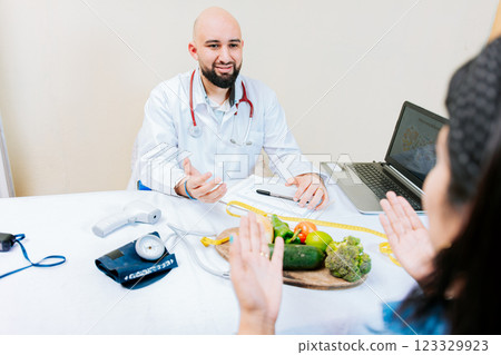 Nutritionist man talking to woman patient in office. Back view of a female patient talking to the nutritionist. Smiling nutritionist explaining to a female patient Nutritionist man talking to woman patient in office. Back view of a female patient talking to the nutritionist. Smiling nutritionist explaining to a female patient 123329923