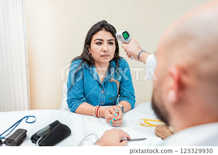 Doctor taking temperature to woman patient in office. Male doctor taking temperature with gun to patient. Doctor measuring temperature with infrared gun to female patient 123329930