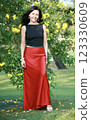 Beautiful brunette woman 51 years old in a satin red long skirt posing against the background of a flowering tree in Goa India 123330609