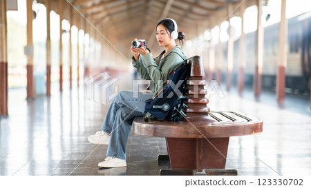 An asian woman is taking a photo with her camera while sitting on the bench in the train station. 123330702