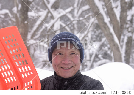 An old man clearing snow in a snowy area 123330898