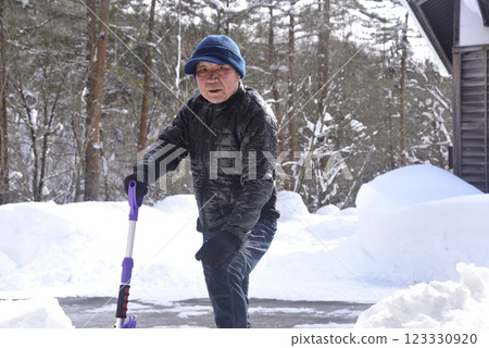 A smiling old man using a snow plow to remove snow in a snowy area A smiling old man using a snow plow to remove snow in a snowy area 123330920