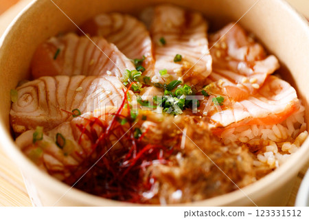 Donburi with sliced salmon on sushi rice in paper container. Healthy take away food. 123331512
