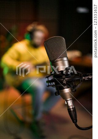 Male singer recording songs by using a studio microphone and and playing guitar in a music recording studio. Performance and show in the music business, streaming and recording music. Male singer recording songs by using a studio microphone and and playing guitar in a music recording studio. Performance and show in the music business, streaming and recording music. 123331617