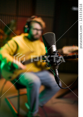 Male singer recording songs by using a studio microphone and and playing guitar in a music recording studio. Performance and show in the music business, streaming and recording music. Male singer recording songs by using a studio microphone and and playing guitar in a music recording studio. Performance and show in the music business, streaming and recording music. 123331618