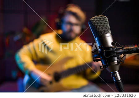 Male singer recording songs by using a studio microphone and and playing guitar in a music recording studio. Performance and show in the music business, streaming and recording music. Male singer recording songs by using a studio microphone and and playing guitar in a music recording studio. Performance and show in the music business, streaming and recording music. 123331620