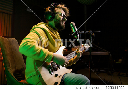Male singer recording songs by using a studio microphone and and playing guitar in a music recording studio. Performance and show in the music business, streaming and recording music. Male singer recording songs by using a studio microphone and and playing guitar in a music recording studio. Performance and show in the music business, streaming and recording music. 123331621