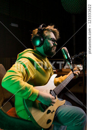 Male singer recording songs by using a studio microphone and and playing guitar in a music recording studio. Performance and show in the music business, streaming and recording music. 123331622