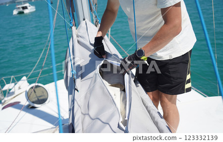 Male captain on deck of sailboat unpacking sails pulling zipper Male captain on deck of sailboat unpacking sails pulling zipper 123332139