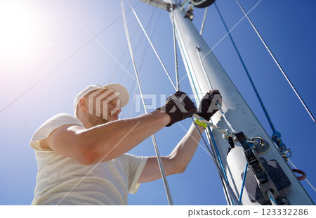 Male captain on deck of sailboat opening sails pulling the rope Male captain on deck of sailboat opening sails pulling the rope 123332286