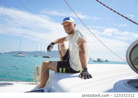 A man is calmly sitting on the deck of a beautiful sailboat A man is calmly sitting on the deck of a beautiful sailboat 123332312