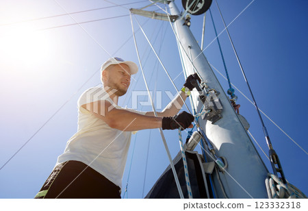 Male captain on deck of sailboat opening sails pulling the rope Male captain on deck of sailboat opening sails pulling the rope 123332318