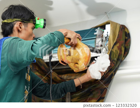 The worker cleans and repairs the air conditioner to ensure it operates properly 123332320