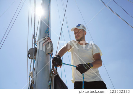 Male captain on deck of sailboat opening sails pulling the rope Male captain on deck of sailboat opening sails pulling the rope 123332323