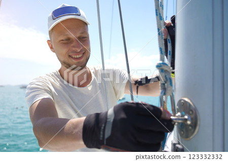 Male captain on deck of sailboat opening sails pulling the rope 123332332
