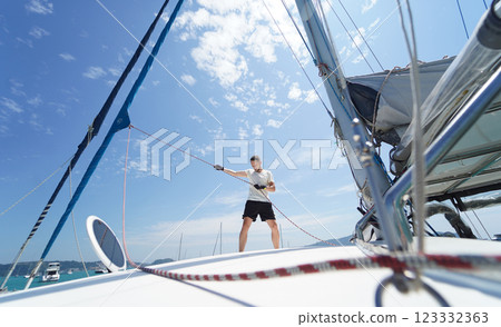 Male captain on deck of sailboat opening sails pulling the rope 123332363