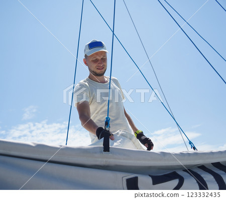 Male captain on deck of sailboat unpacking sails pulling zipper Male captain on deck of sailboat unpacking sails pulling zipper 123332435