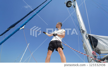 Male captain on deck of sailboat opening sails pulling the rope Male captain on deck of sailboat opening sails pulling the rope 123332436