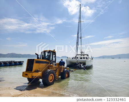 Yellow tractor is pulling a boat out of the water in a beautiful coastal area 123332461