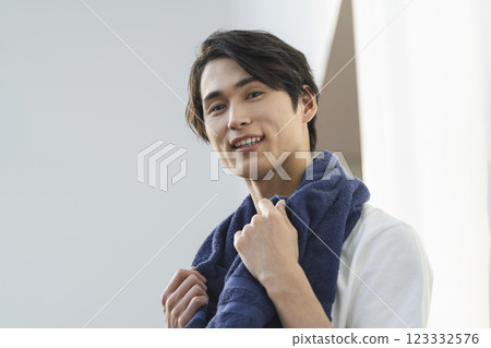 A man in his 20s smiling and looking at the camera with a towel draped over his shoulders 123332576