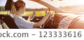 Young woman sitting behind the wheel in a car and watching in a smartphone. 123333616