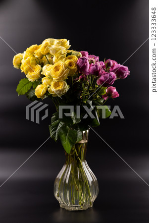 black background with iridescent light there a figured glass vase with a large bouquet of yellow and pink peony roses a gift for a beloved woman a favorite color home decoration first date March 8th 123333648